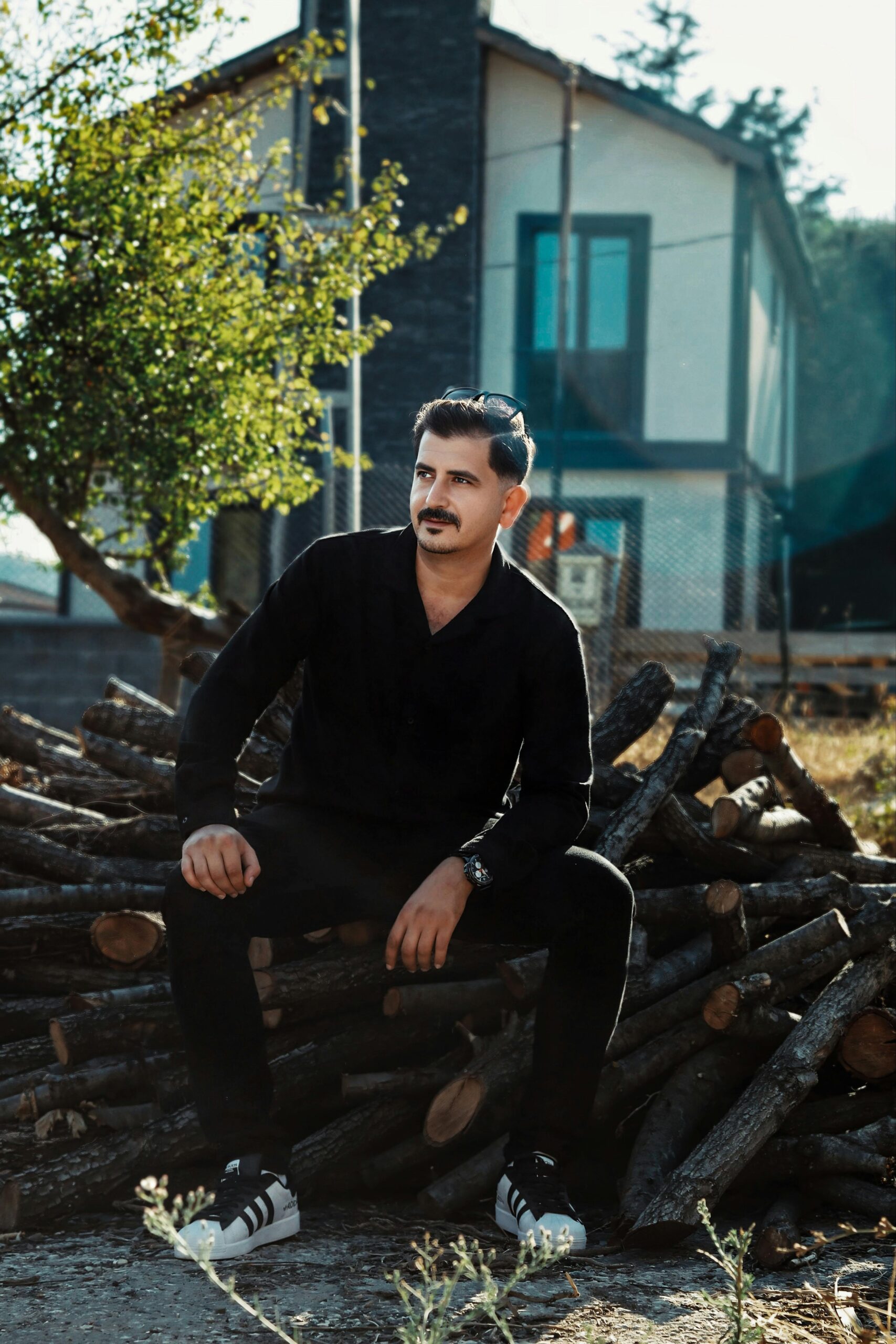 Young man relaxing on a stack of logs outdoors in front of a modern house.